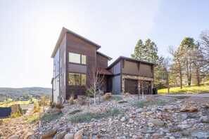 A modern two-story house with a garage, surrounded by a rocky landscape and trees.