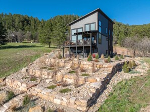 A modern two-story house with a stone foundation, surrounded by a natural landscape.