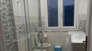 A bathroom with a glass shower enclosure, two toilets, a sink, and a washing machine. - Vacation home Perla Marina (Porto Empedocle)