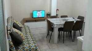 A modern living room with a sofa, a dining table, and a TV. - Vacation home Perla Marina (Porto Empedocle)