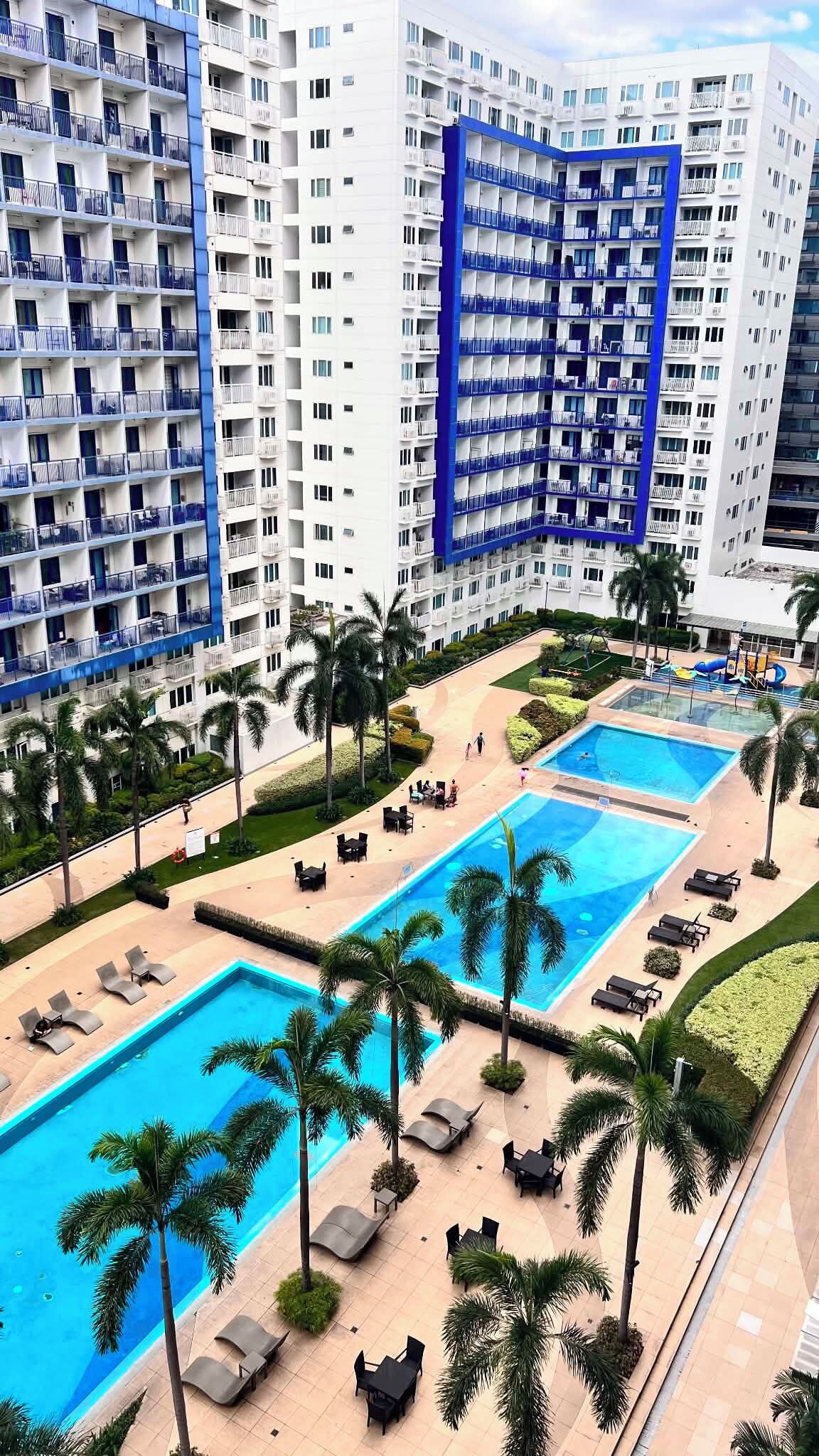 A hotel with multiple swimming pools, palm trees, and a large building with balconies.