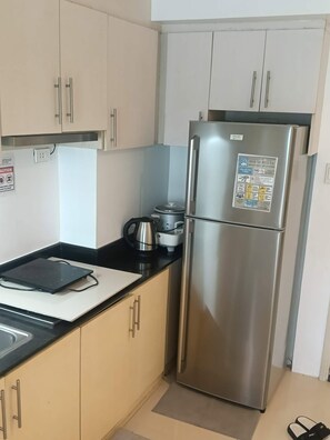 A kitchen with a stainless steel refrigerator, a kettle, and a portable stove on the countertop. - Spacious 2BR at Sea Residences Near MOA - Family Stay (Pasay)