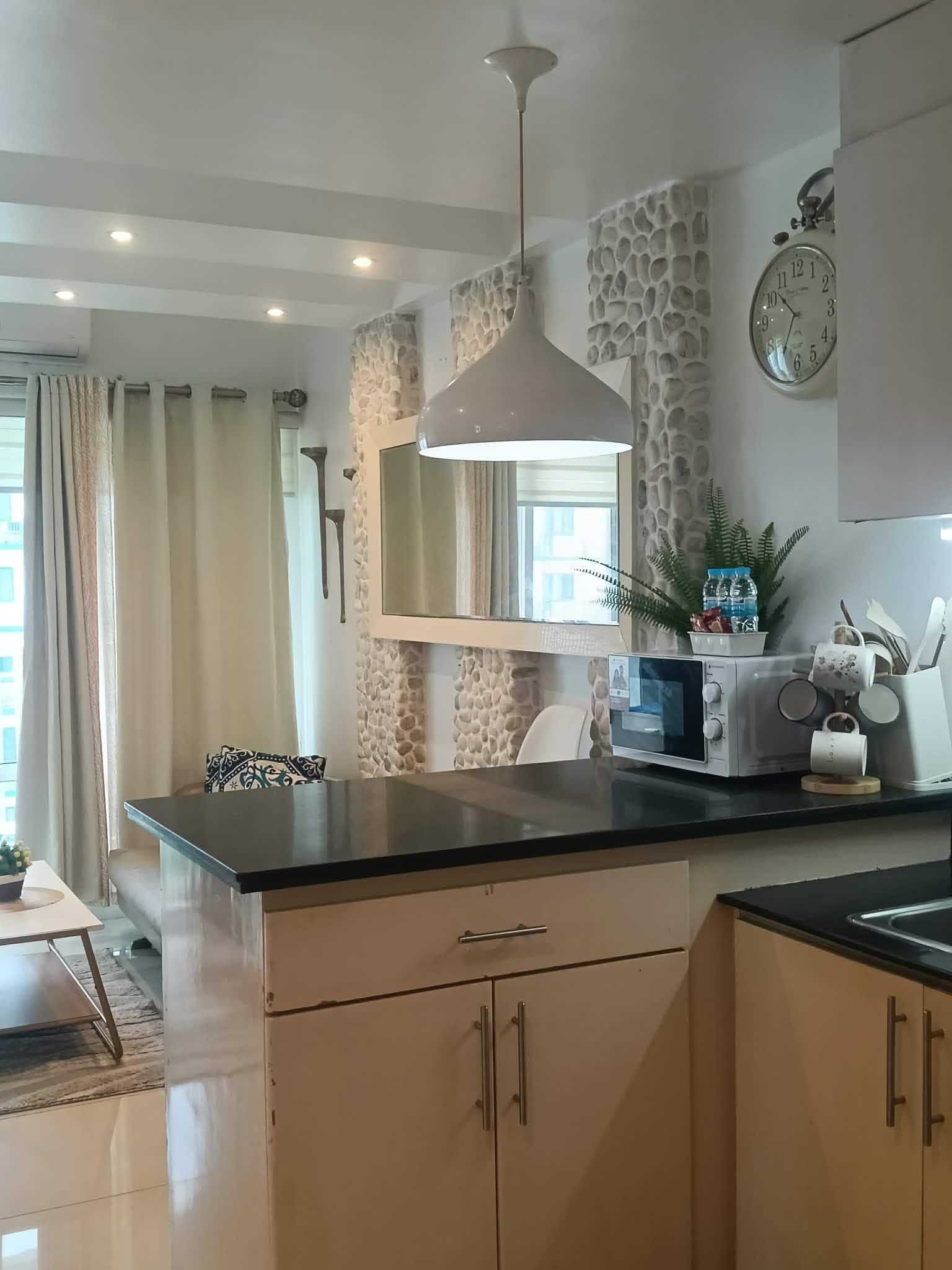 A modern kitchen with a black countertop, white cabinets, a hanging light fixture, and a stone accent wall.