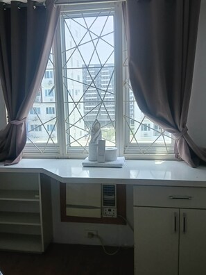A room with a window, curtains, a desk, and a view of buildings outside. - Spacious 2BR at Sea Residences Near MOA - Family Stay (Pasay)