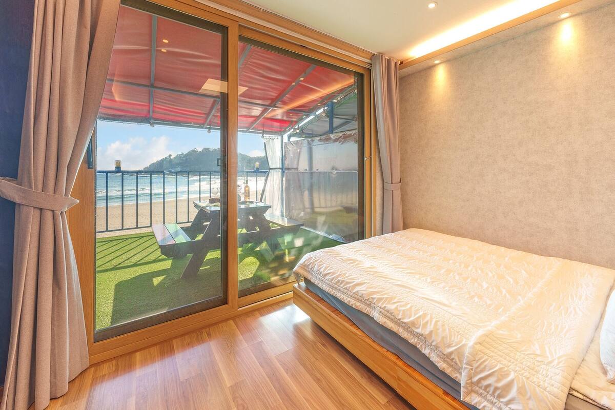 Une chambre dotée d’une grande porte-fenêtre coulissante donnant sur un balcon avec vue sur la plage et surmontée d’un auvent rouge.