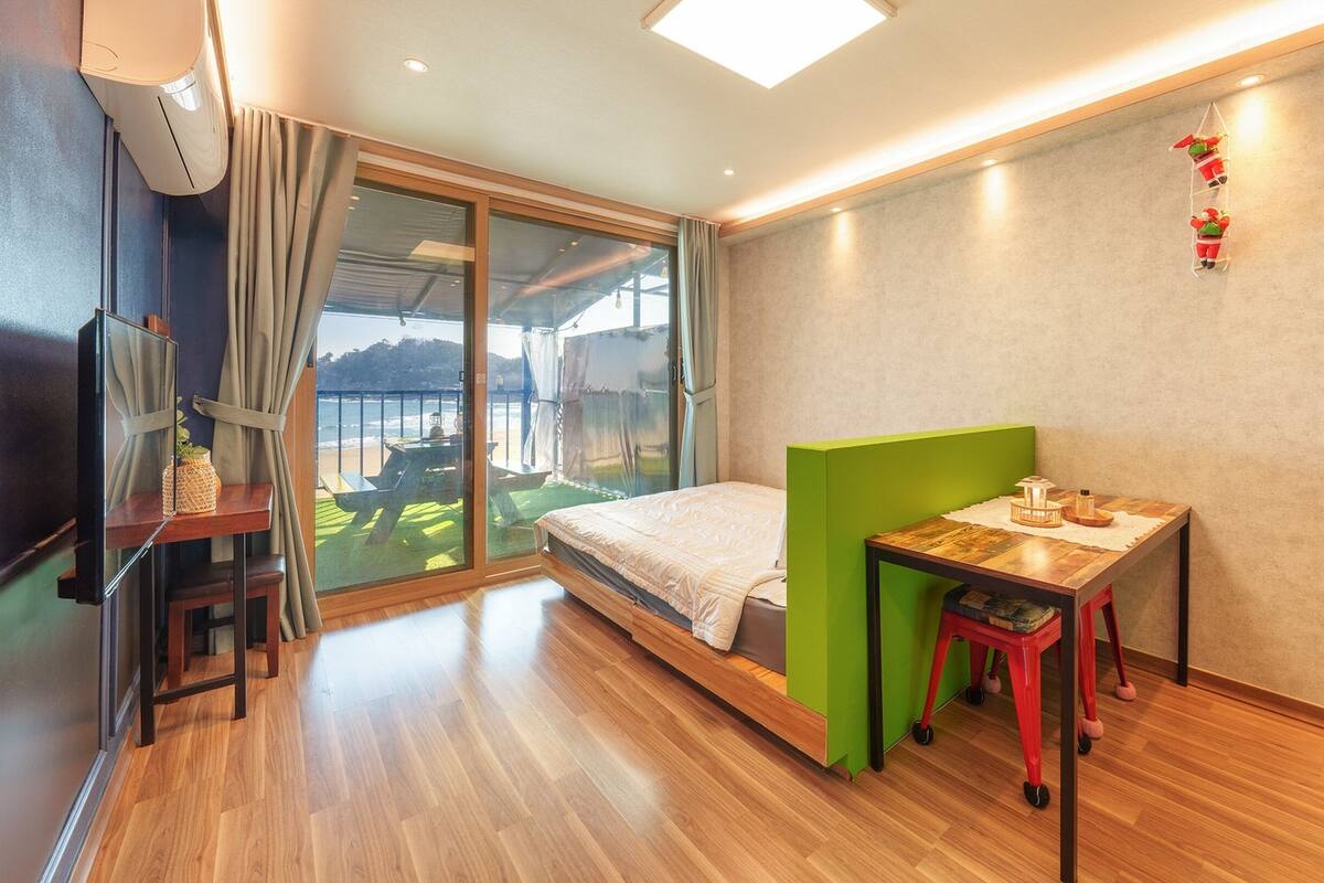 Une chambre d’hôtel moderne équipée d’un lit, d’une petite table, d’une télévision et d’un balcon avec vue sur la plage.