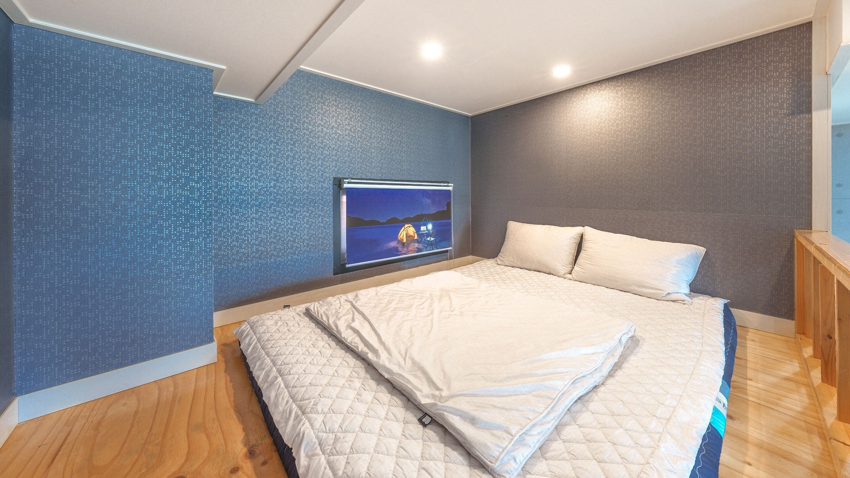 Une chambre avec un grand lit, un téléviseur fixé au mur et un plancher en bois.