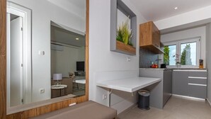 A modern kitchen with a built-in bench, grey cabinets, and a window with a view of trees. - Apartman Helena (Crikvenica)