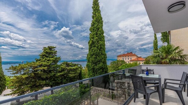 A balcony with a glass railing overlooking a scenic view of the sea and trees. - Apartman Helena (Crikvenica)