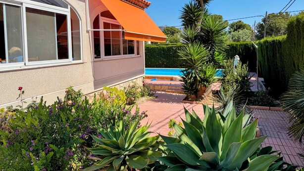 Una casa circondata da vegetazione, con una piscina e un cielo azzurro.