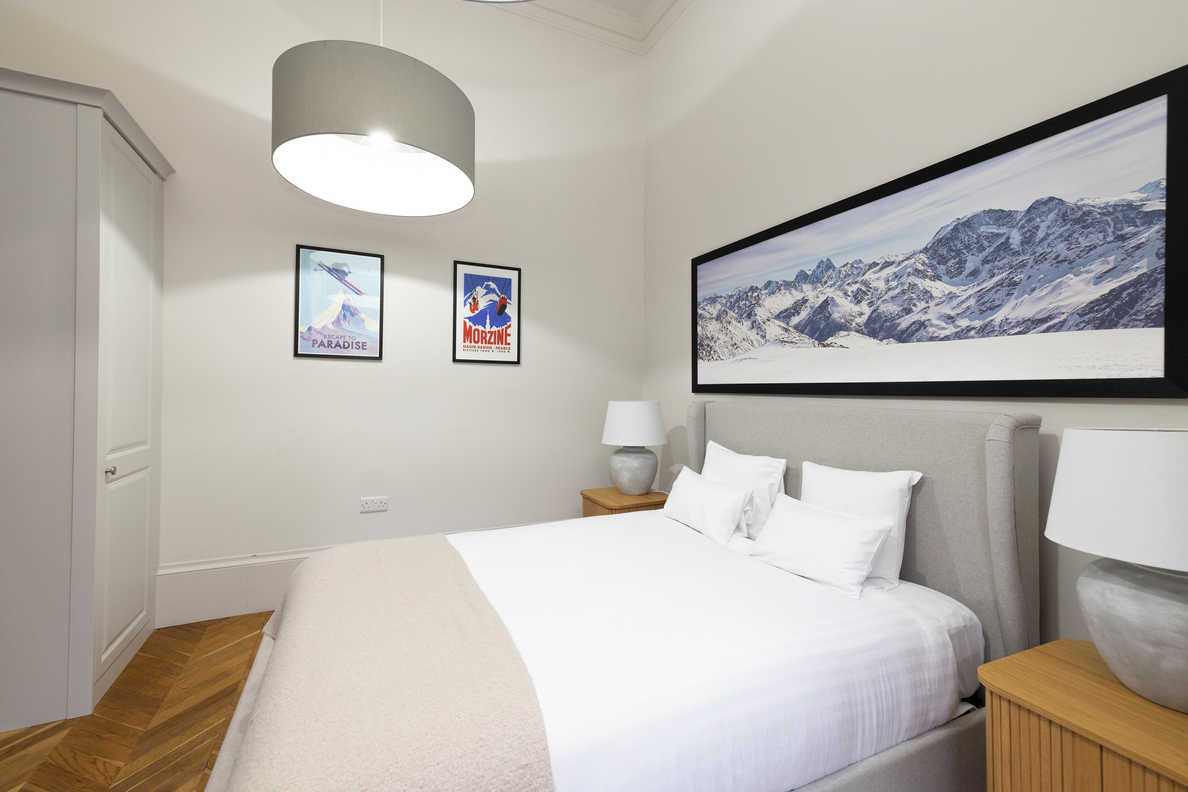 A bedroom with a bed, a nightstand, a lamp, and two framed pictures on the wall.