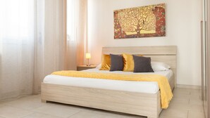 Een net opgemaakt bed met een houten hoofdbord, een gele plaid en twee kussens.