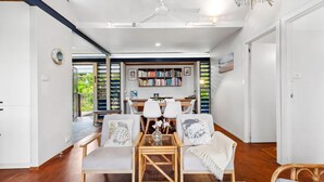 A modern dining area with a wooden table, white chairs, and a bookshelf filled with books.