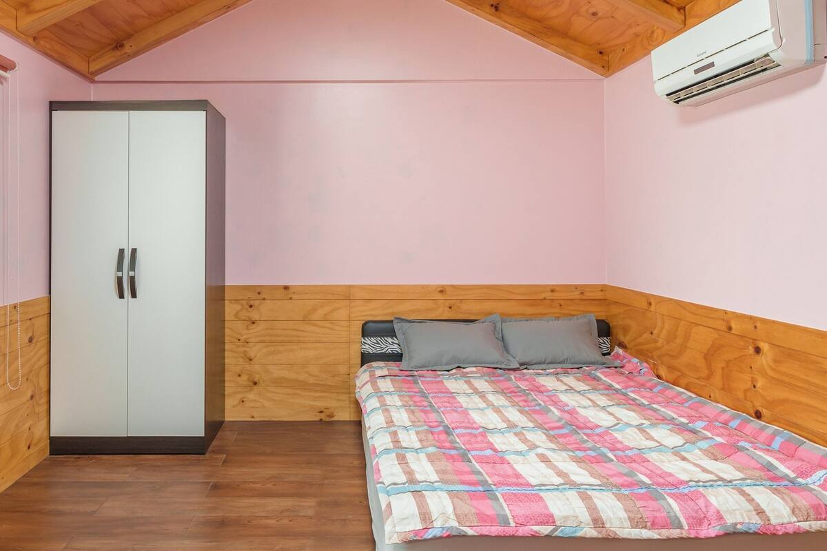 A bedroom with a wooden wardrobe, a bed with a patterned quilt, and an air conditioning unit on the wall.
