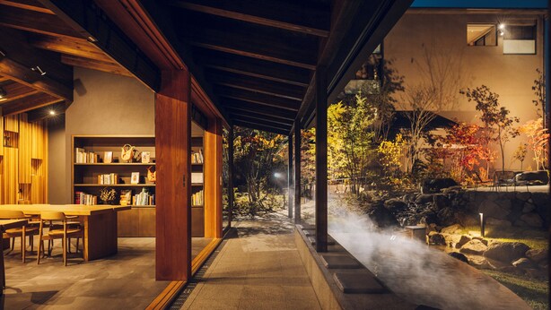 Ein modernes Interieur mit einem Essbereich aus Holz, einer Bücherwand und Blick auf einen Garten mit Thermalquelle.