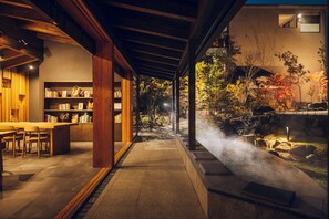 Ein modernes Interieur mit einem Essbereich aus Holz, einer Bücherwand und Blick auf einen Garten mit Thermalquelle.