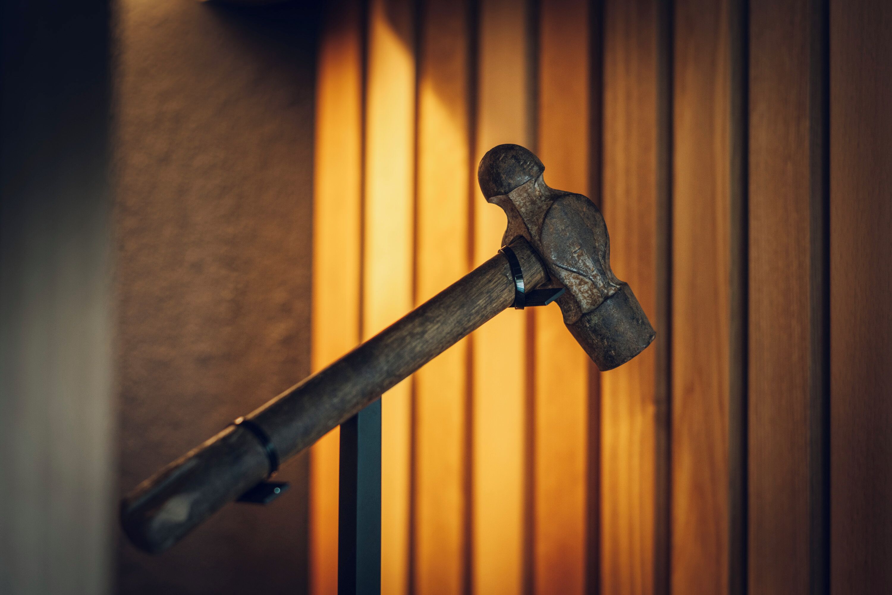 A hammer hanging on a wall with vertical wooden slats in the background.