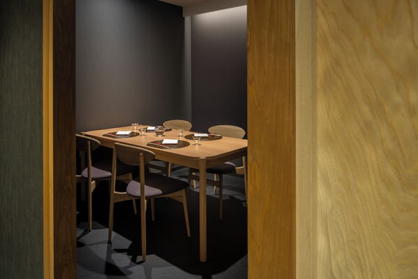 A conference room with a wooden table and chairs, equipped with a projector and a screen.