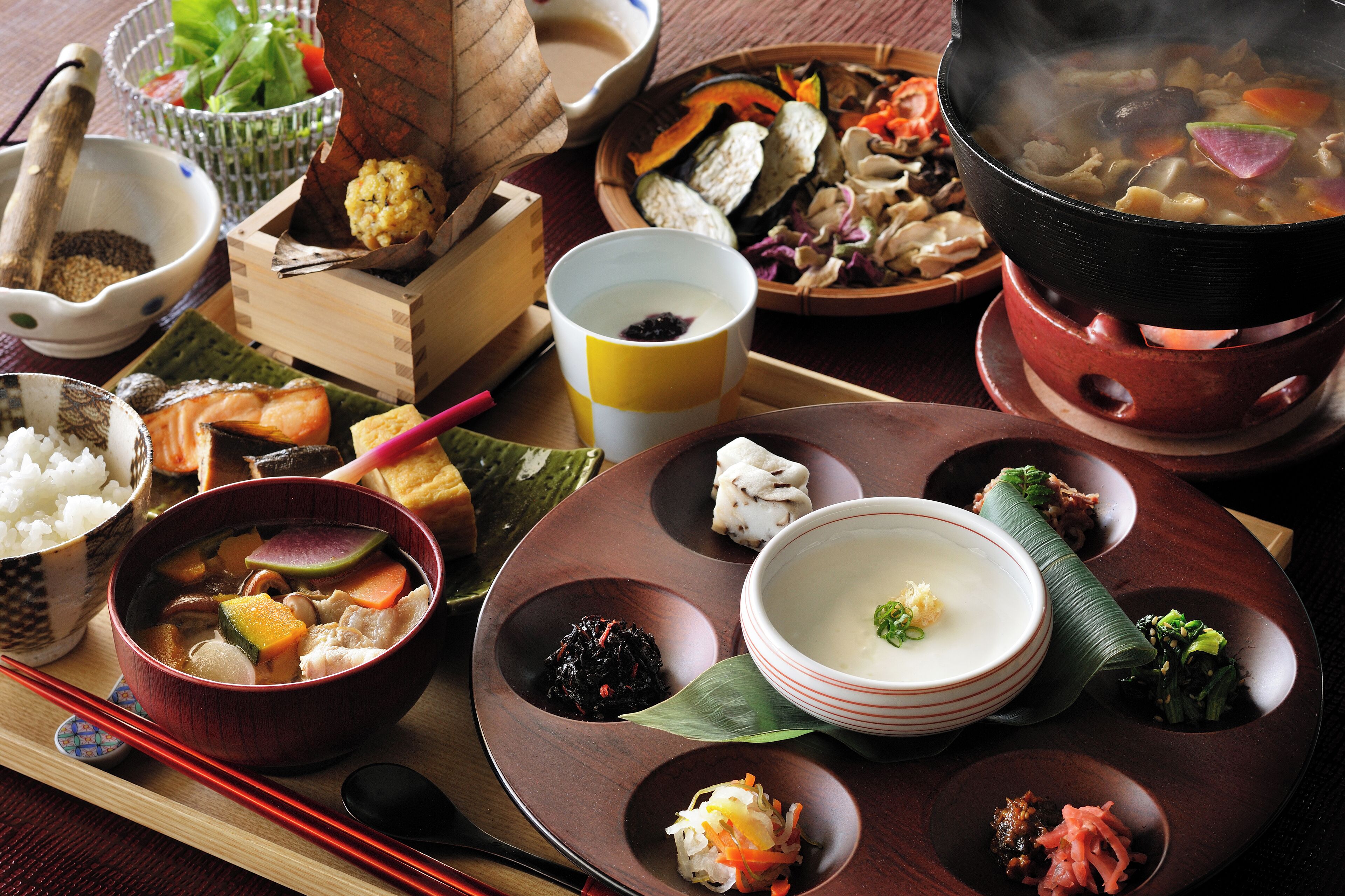A variety of traditional Japanese dishes served on a wooden table, including a pot of soup, bowls of rice, and assorted side dishes.