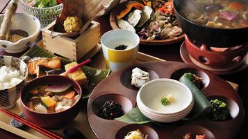 A variety of traditional Japanese dishes served on a wooden table, including a pot of soup, bowls of rice, and assorted side dishes.