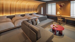 Ein modernes Hotelzimmer mit gewölbter Decke, einer Couch, einem roten Tisch mit Lampe sowie einem Schreibtisch und einem Stuhl.