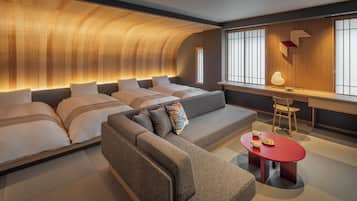 A modern hotel room with a curved ceiling, a sofa, a red table with a lamp, and a desk with a chair.