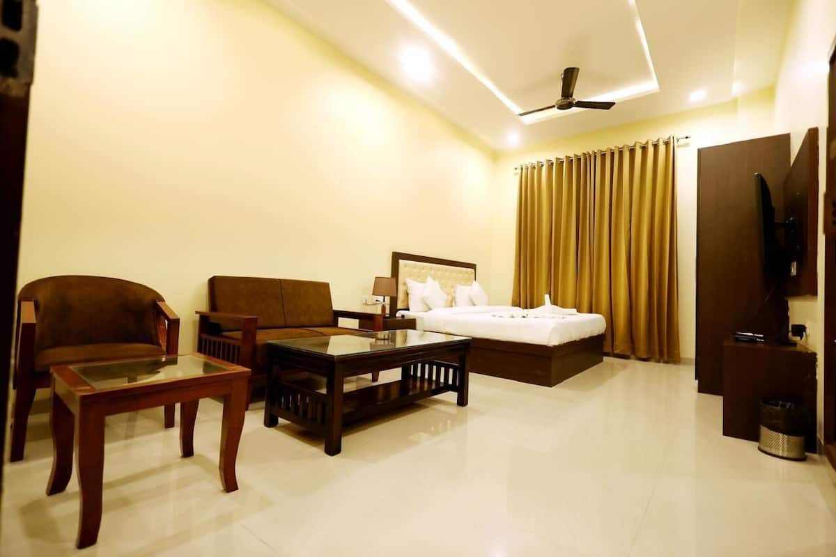 A hotel room with a bed, two sofas, a coffee table, a TV, and a ceiling fan.