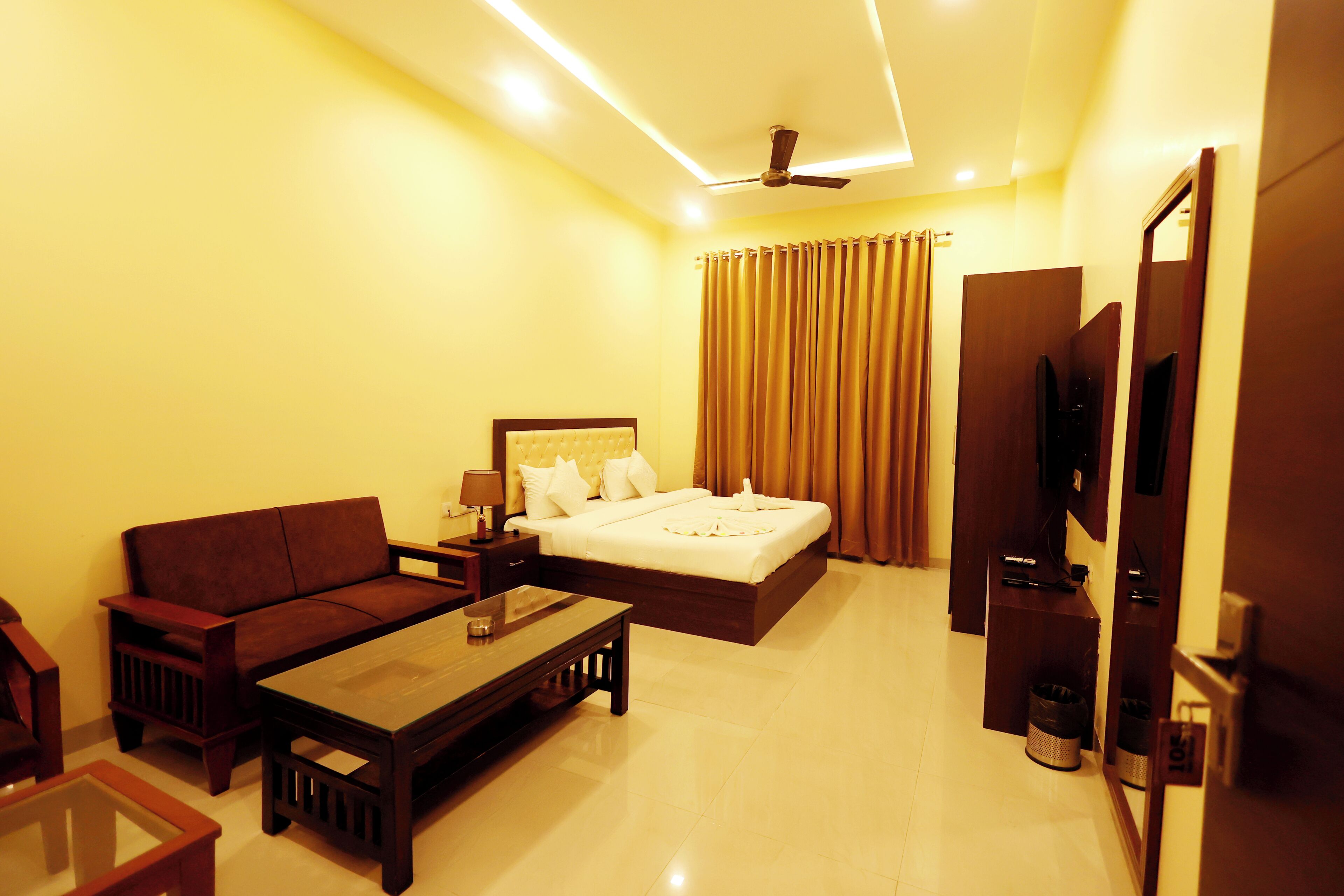 A hotel room with a bed, a sofa, a coffee table, a TV, and a ceiling fan.