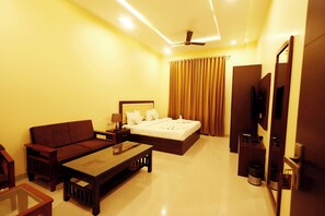A hotel room with a bed, a sofa, a coffee table, a TV, and a ceiling fan. - Hari Mahal Resort (Behror)