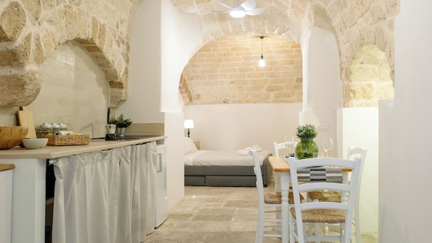 A cozy kitchen with a stone archway leading to a dining area, featuring a bed and a small table with chairs. - Travel Old Bari (Bari)