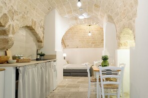 A cozy kitchen with a stone archway leading to a dining area, featuring a bed and a small table with chairs. - Travel Old Bari (Bari)