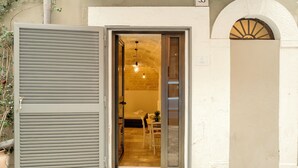 A doorway with a sliding glass door leading to an interior space with a brick wall, a hanging light fixture, and a small table with chairs. - Travel Old Bari (Bari)