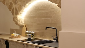 A kitchen with a stone arch, a sink, and a countertop with a basket and a coffee maker. - Travel Old Bari (Bari)