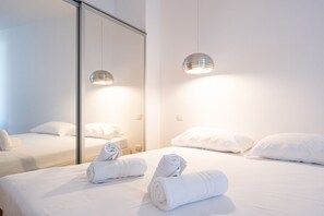 A hotel room with a large mirror, two beds with white linens, and two pendant lights.