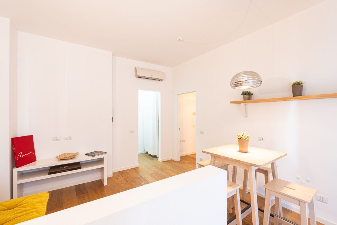 Een modern, minimalistisch woongedeelte met een wit kleurenschema, een houten eettafel en een bank.