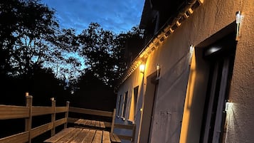 Un patio esterno in legno con tavoli da picnic, un edificio dalla facciata strutturata e una porta con finestra.
