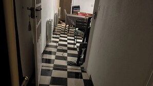 Un passadís estret amb un paviment de quadradets blancs i negres, que condueix a una zona de menjador amb taula i cadire.