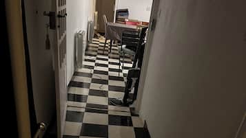 Un pasillo estrecho con suelo a cuadros blanco y negro que conduce a un comedor con mesa y sillas.