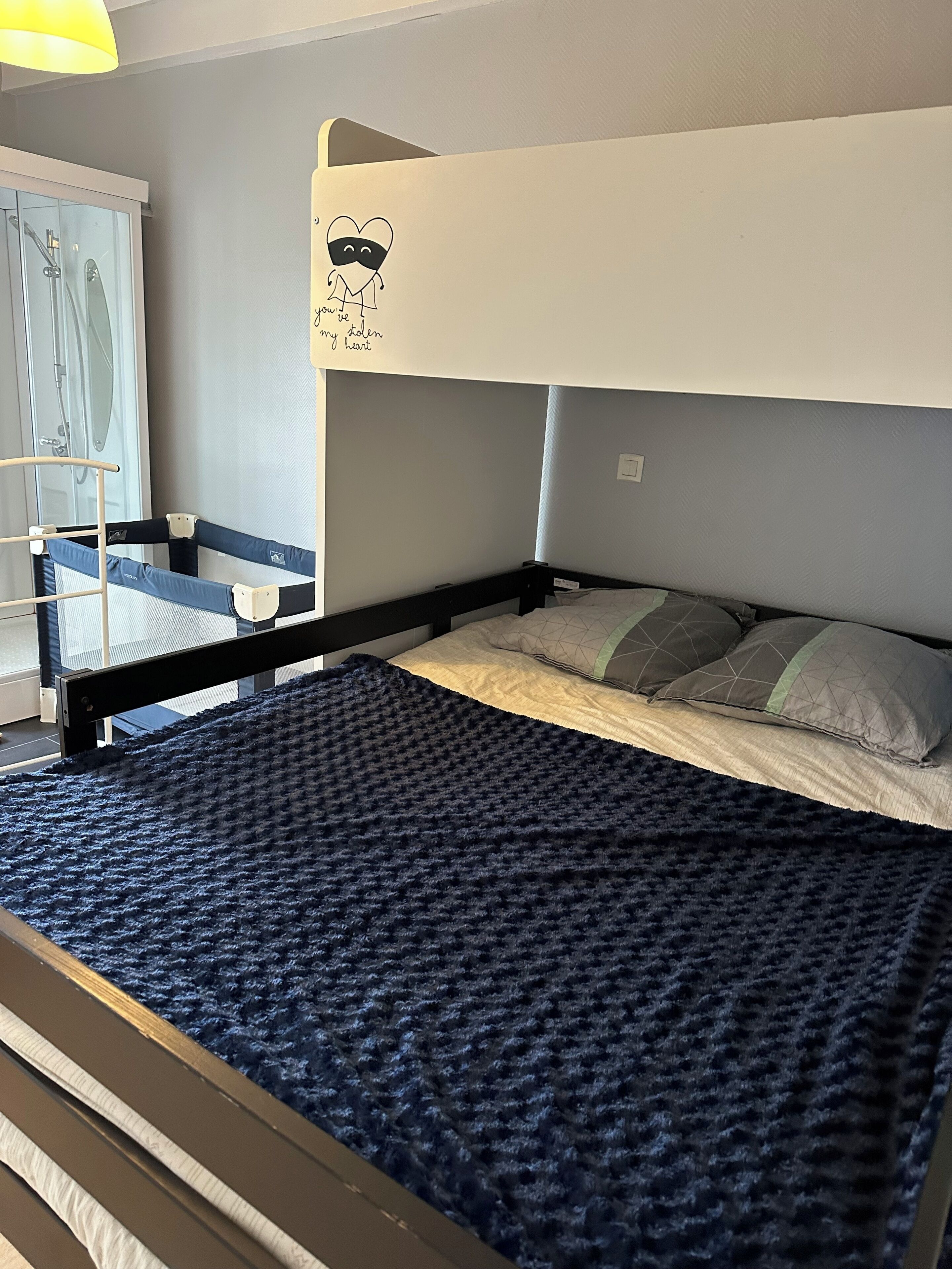 Letto a castello con coperta blu, una piccola scala e una finestra con vista su un box doccia.