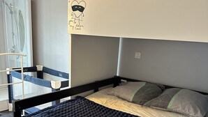 Un llit superposat amb llençol blau, una petita escala i una finestra amb vista a la dutxa.