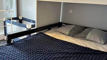 Letto a castello con coperta blu, una piccola scala e una finestra con vista su un box doccia.
