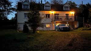 Una casa de dos pisos amb un cotxe a la entrada, envoltada d'arbres i un jardí ben cuidat.