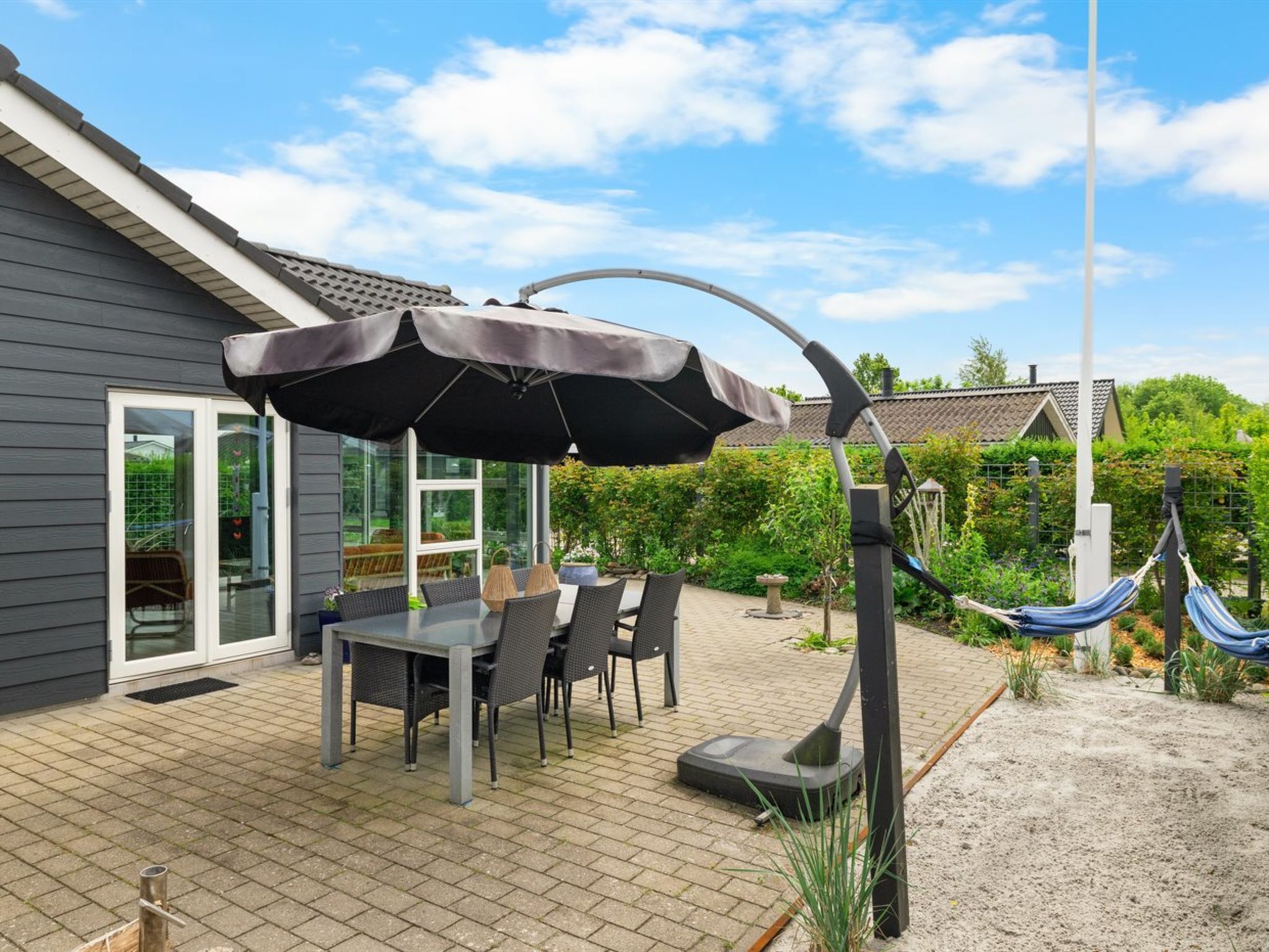 An outdoor patio with a table and chairs, a large umbrella, a hammock, and a house in the background.