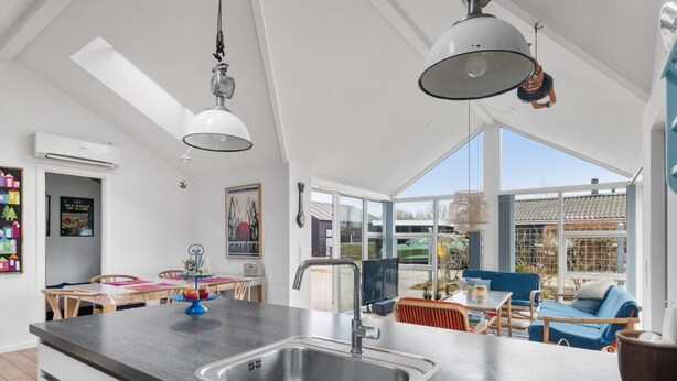 Una cocina moderna con una isla grande, un comedor con mesa y sillas, y vistas al exterior a través de amplios ventanales.