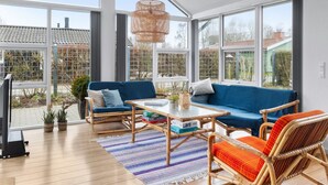 Una habitación amplia con ventanas grandes, un sofá azul, sillones de mimbre y una mesa de centro.