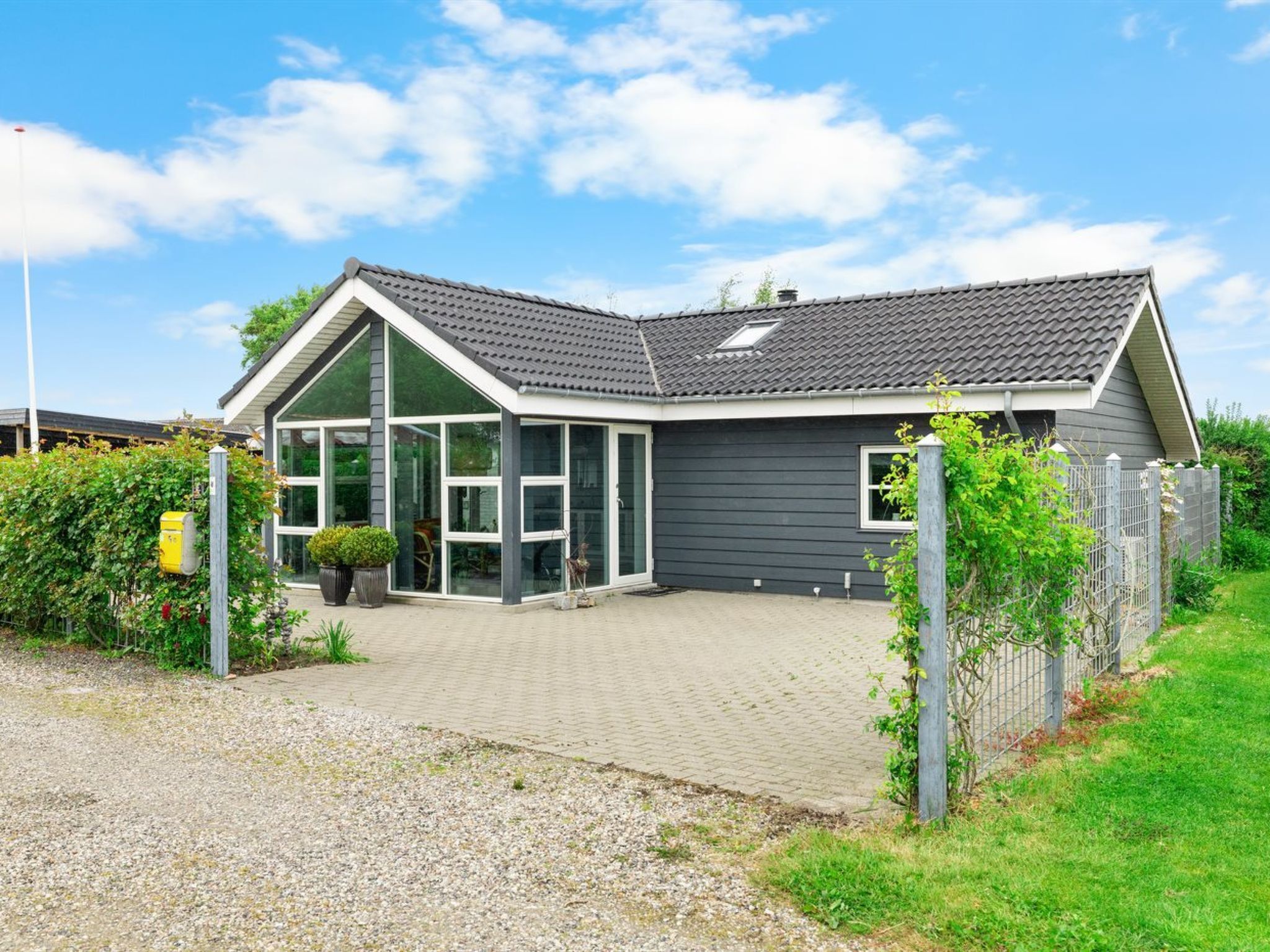 A modern house with a sloped roof, large glass windows, and a paved driveway.