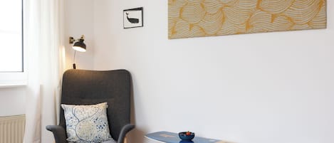 A room with a chair, a table, a wall-mounted lamp, and a framed picture.