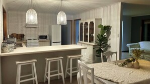A modern kitchen with a central island, white bar stools, and pendant lighting.