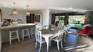 A modern kitchen with a central island, bar stools, and a dining area with a wooden table and white chairs.