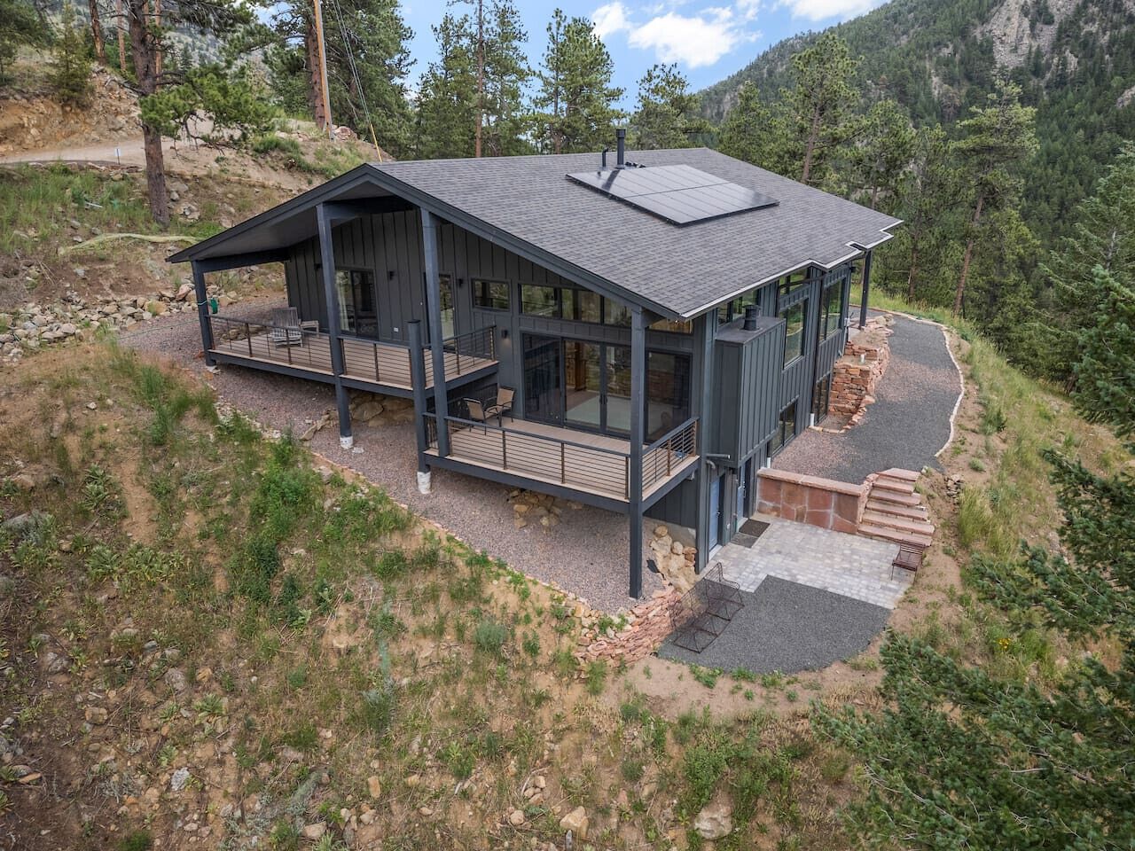 A modern cabin with a large deck, built into a hillside with a view of the surrounding forest.